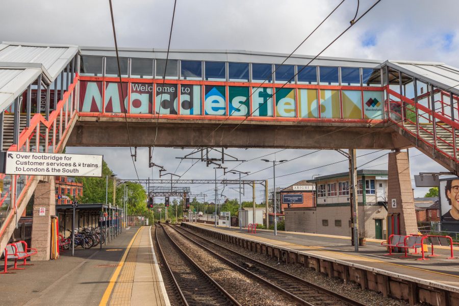 Footbridge across the tracks at Macclesfield Station, with a large Macclesfield sign on its exterior.